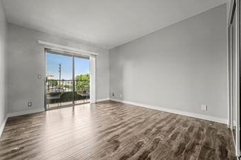 A room with wooden flooring and a sliding glass door leading to a balcony.
